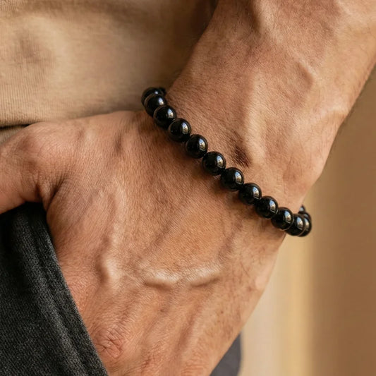 Gros plan sur le poignet d'un homme portant un bracelet en pierres d'Onyx noir, la main dans la poche. Un bijou masculin porteur de sens.
