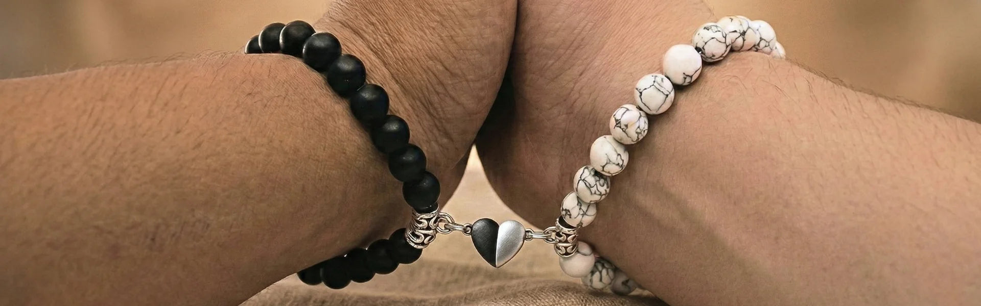 Deux poignets unis portant un bracelet couple distance en pierres naturelles d'onyx noir et howlite blanche avec un cœur aimanté