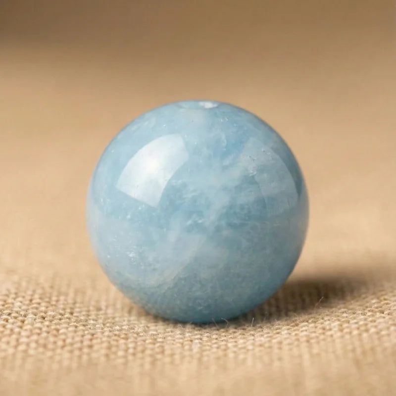 Gros plan sur une perle polie en aigue-marine véritable. Pierre naturelle douce aux nuances bleu clair et inclusions organiques sur fond texturé.