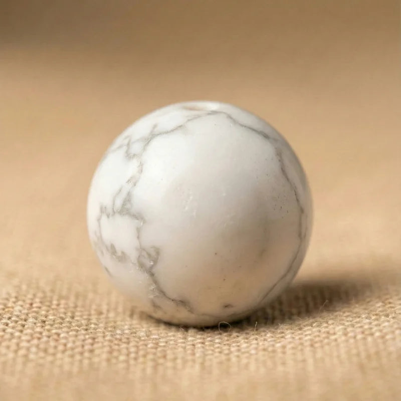 Vue rapprochée d'une perle de Howlite blanche aux marbrures grises naturelles, illustrant l'élégance du minimalisme minéral.