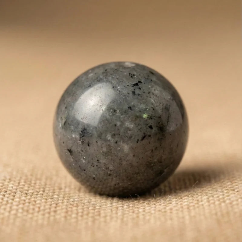 Macro d'une perle de Labradorite grise aux nuances sombres et reflets métalliques, symbole de résilience et de caractère brut.