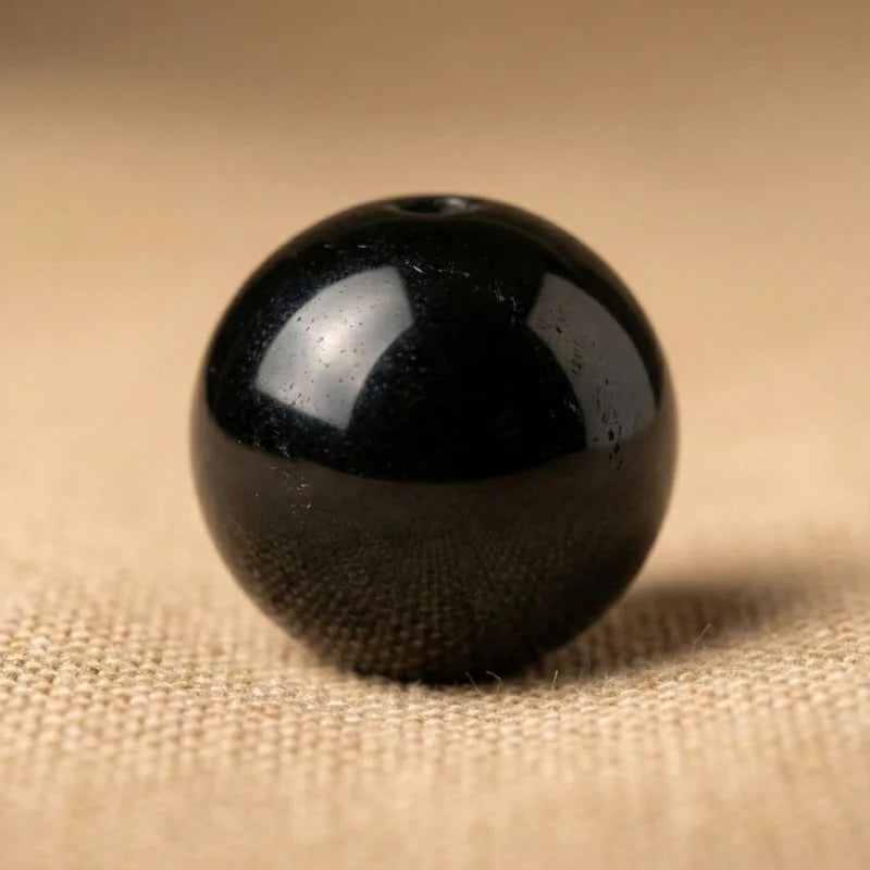 Gros plan macro d'une perle d'Onyx noir poli aux reflets brillants, révélant la profondeur et la force brute du minéral Antaluna.