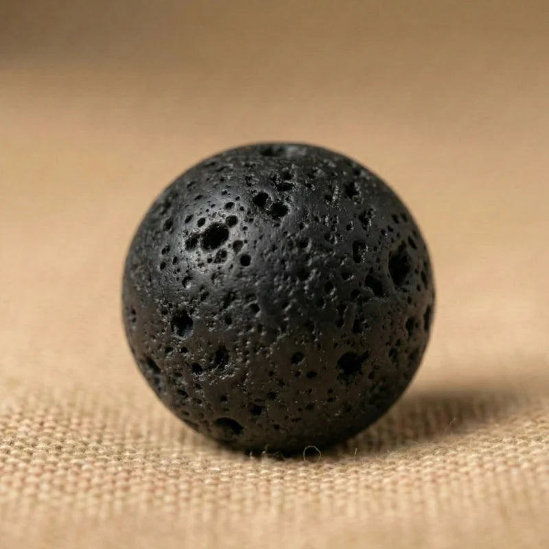 Gros plan sur une perle ronde en pierre de lave naturelle noire. Minéral brut à la texture poreuse, idéal pour les bracelets de lithothérapie.