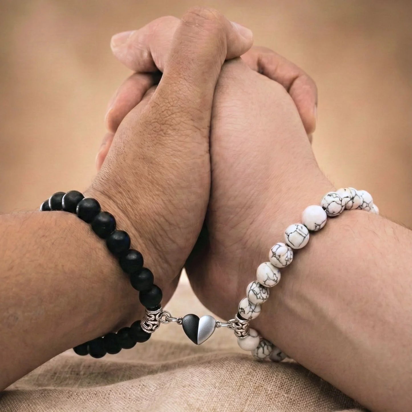 Vue rapprochée de mains qui se tiennent et portant les bracelets couples AMORE. Le coeur aimanté rapproche les bracelets.