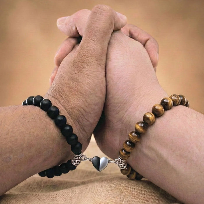 Vue rapprochée de mains qui se tiennent et portant les bracelets couples de distance AMORE brun. Le coeur aimanté rapproche les bracelets.