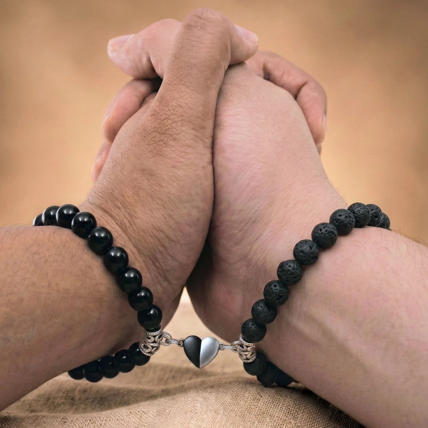 Vue rapprochée de mains qui se tiennent et portant les bracelets couples de distance AMORE noir. Le coeur aimanté rapproche les bracelets.