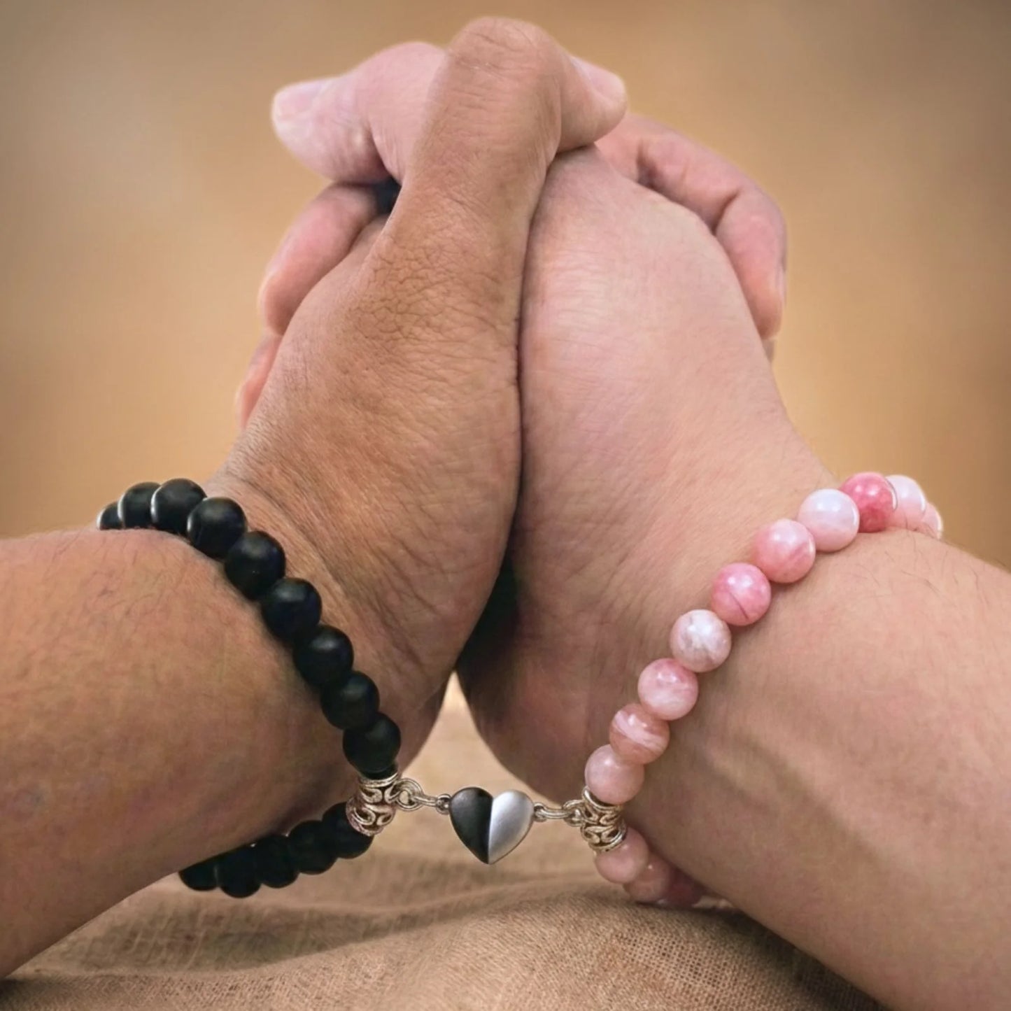 Vue rapprochée de mains qui se tiennent et portant les bracelets couples de distance AMORE rose. Le coeur aimanté rapproche les bracelets.