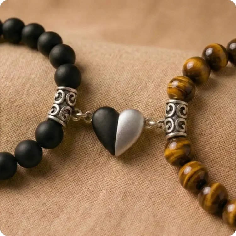 Bracelets pour couple à distance en minéraux véritables. L'image montre l'union magnétique d'un bracelet en Onyx noir mat et d'un bracelet en Œil de Tigre aux reflets dorés, liés au centre par un cœur bicolore noir et argenté.