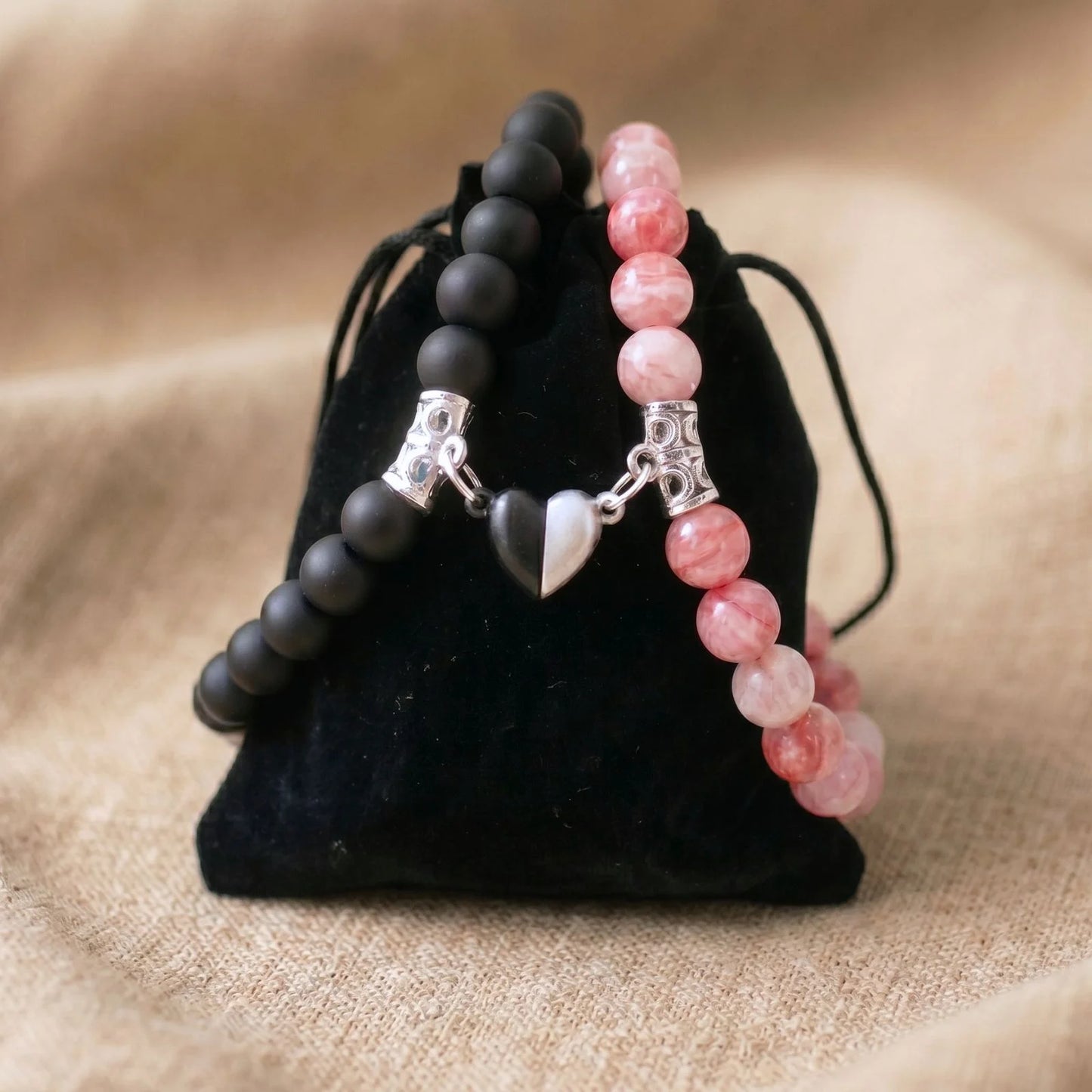 Bracelet couple AMORE en Jade Rose et Onyx posé sur un pochon noir.