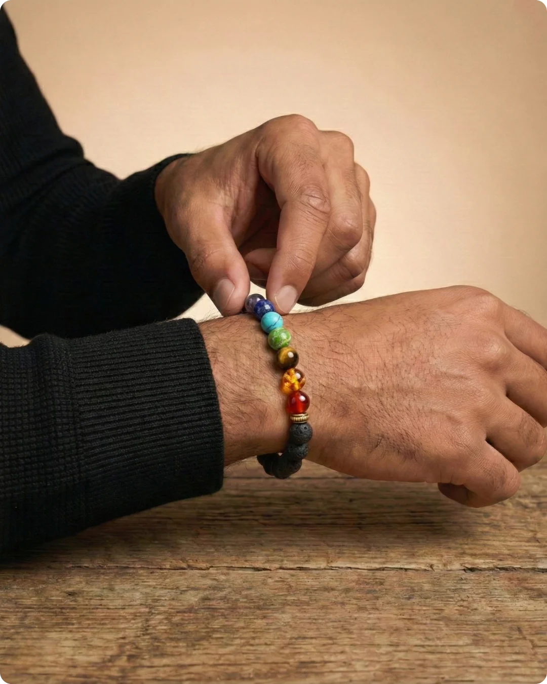 Homme ajustant un bracelet 7 chakras à son poignet. Bijou d'équilibre composé de perles brutes en pierre de lave noire et de sept pierres naturelles colorées.