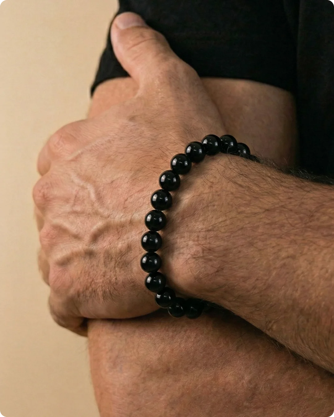 Gros plan sur le bras croisé d'un homme portant un bracelet minimaliste en perles d'onyx noir poli. Un accessoire en pierres naturelles véritables, symbole d'ancrage et d'élégance masculine.