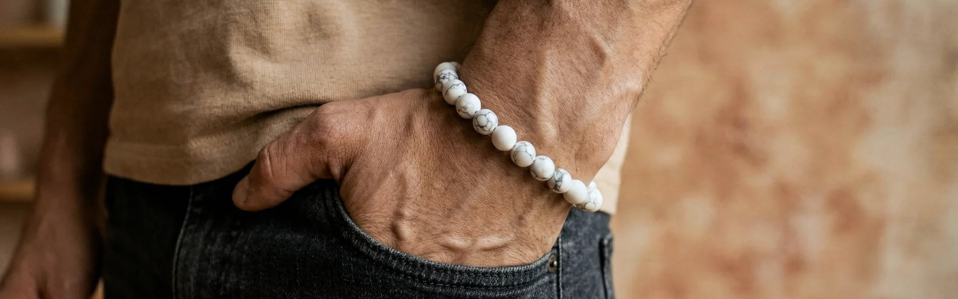 Gros plan sur un poignet masculin portant un bracelet homme en pierre naturelle de howlite blanche, main dans la poche.