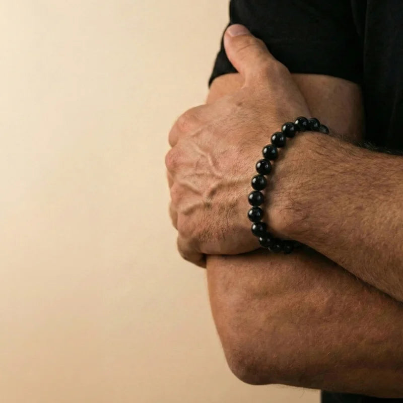 Homme aux bras croisés arborant un bracelet en Onyx noir, un bijou symbolique représentant la force tranquille et le retour à l'essentiel.