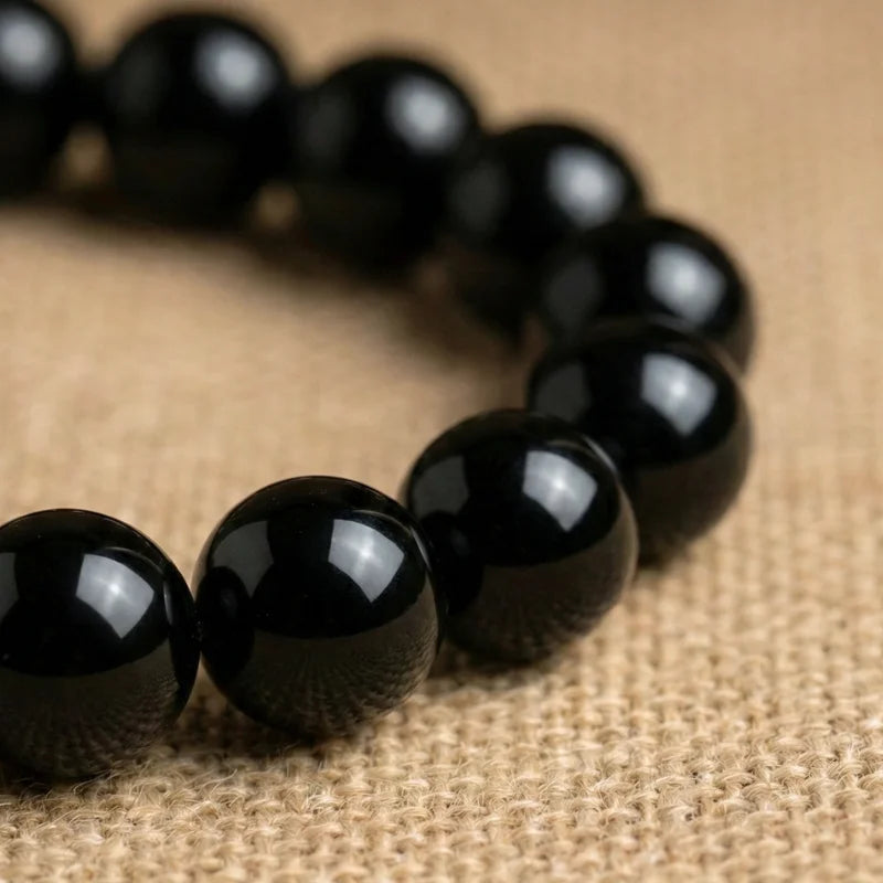 Détail en plan rapproché des perles lisses et brillantes d'un bracelet en Onyx noir, soulignant la pureté de la pierre naturelle.