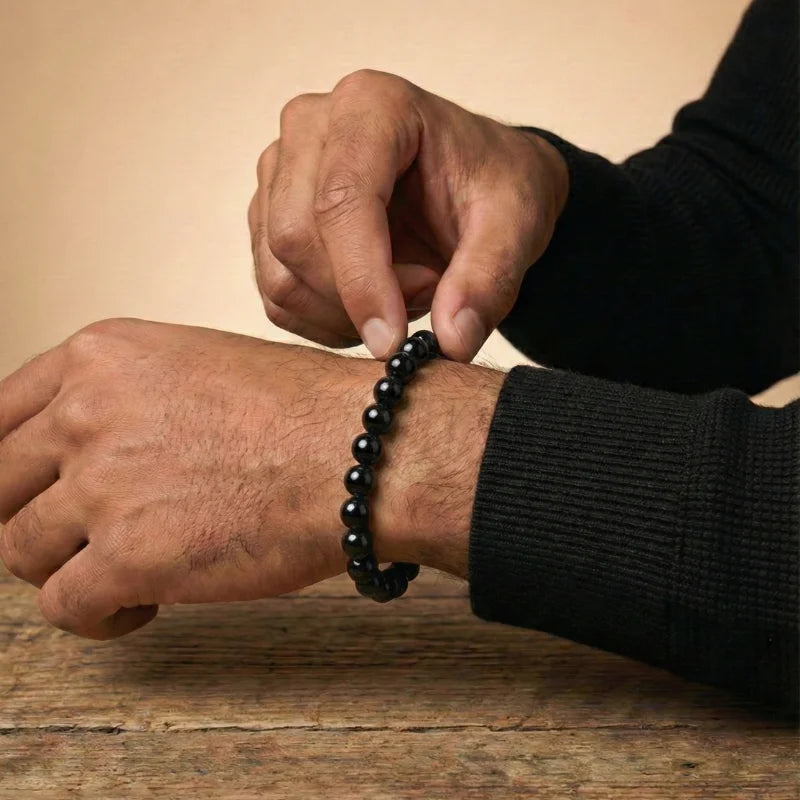 Homme ajustant à deux mains son bracelet en perles d'Onyx noir naturel, au-dessus d'une table en bois brut.